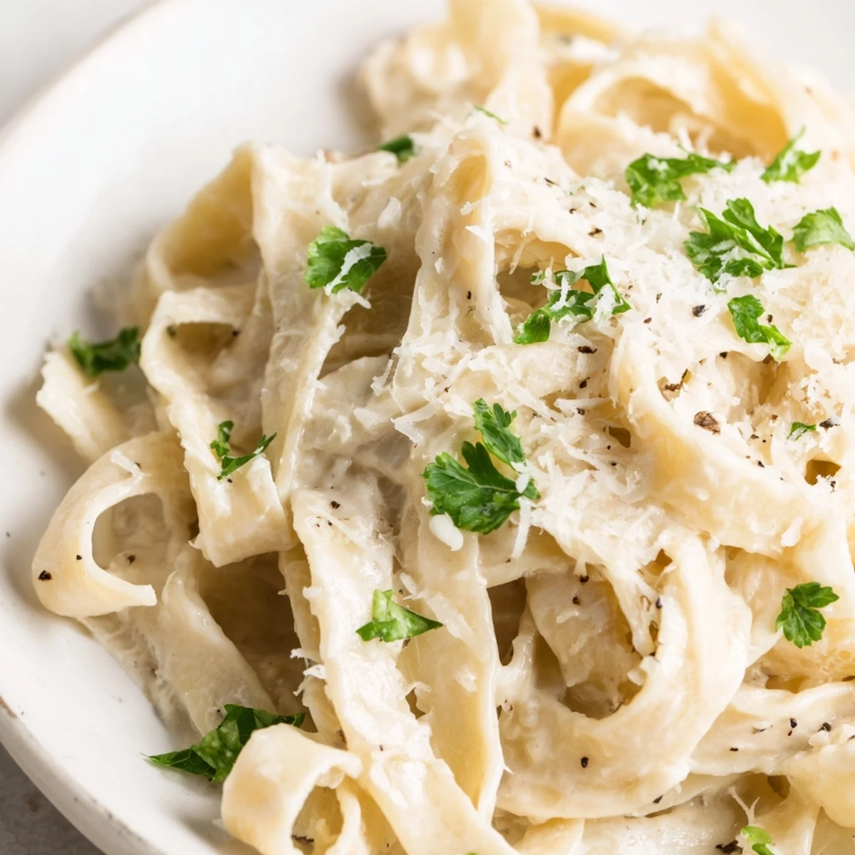 Creamy Sauce over Pasta served in a white bowl, with silky Parmesan sauce clinging to fettuccine and fresh parsley garnish.