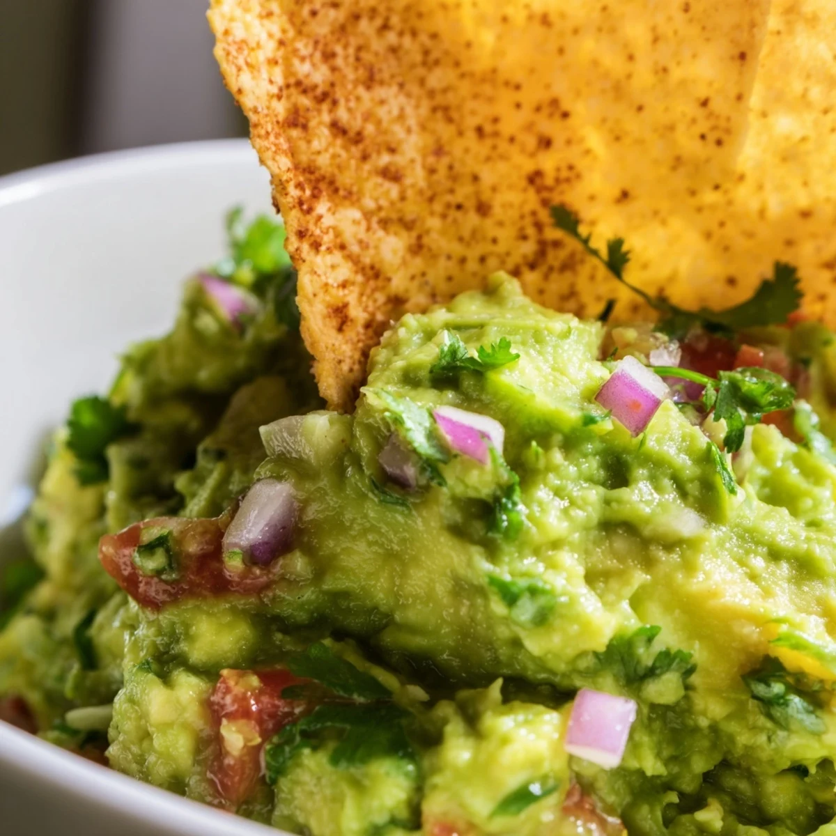 Colorful Big Game Guacamole in a rustic bowl, surrounded by warm, crunchy tortilla chips on a wooden serving platter.