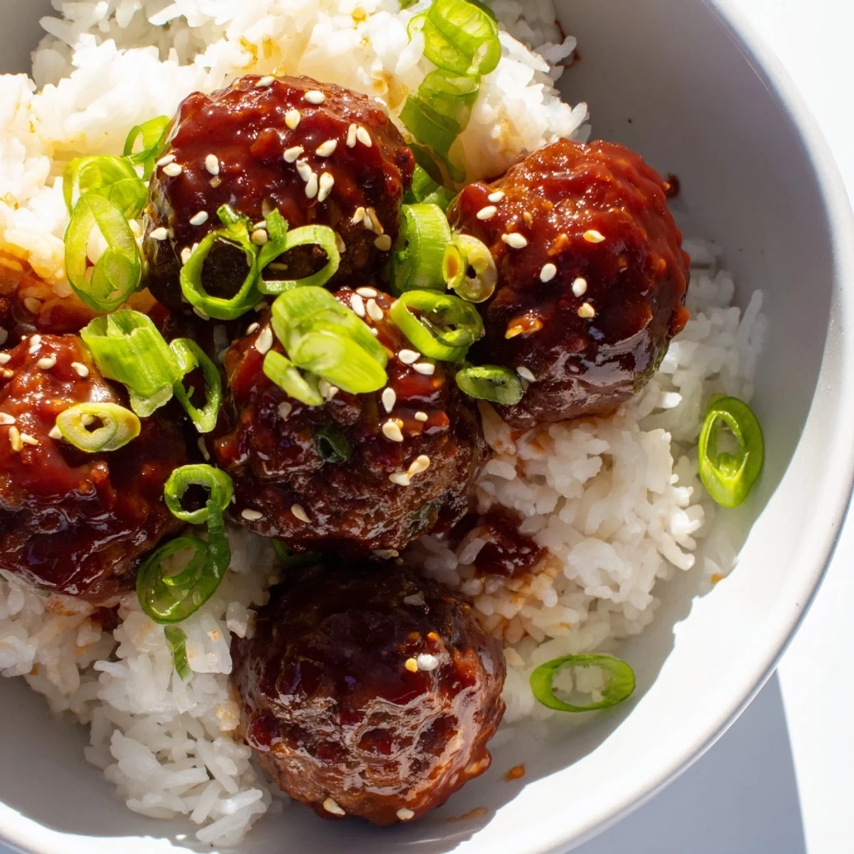 Golden-baked spicy Sriracha beef meatballs on steamed rice garnished with green onions and sesame.