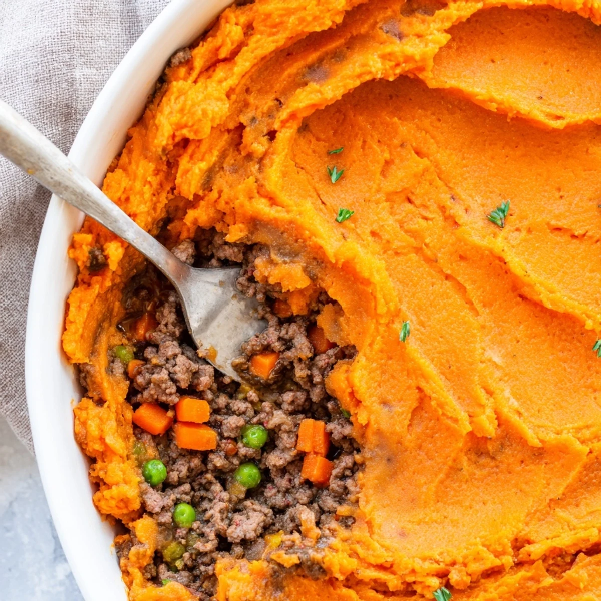 A fork lifts a portion of this savory sweet potato shepherds pie, revealing its rich, bubbling filling and golden-brown top.  