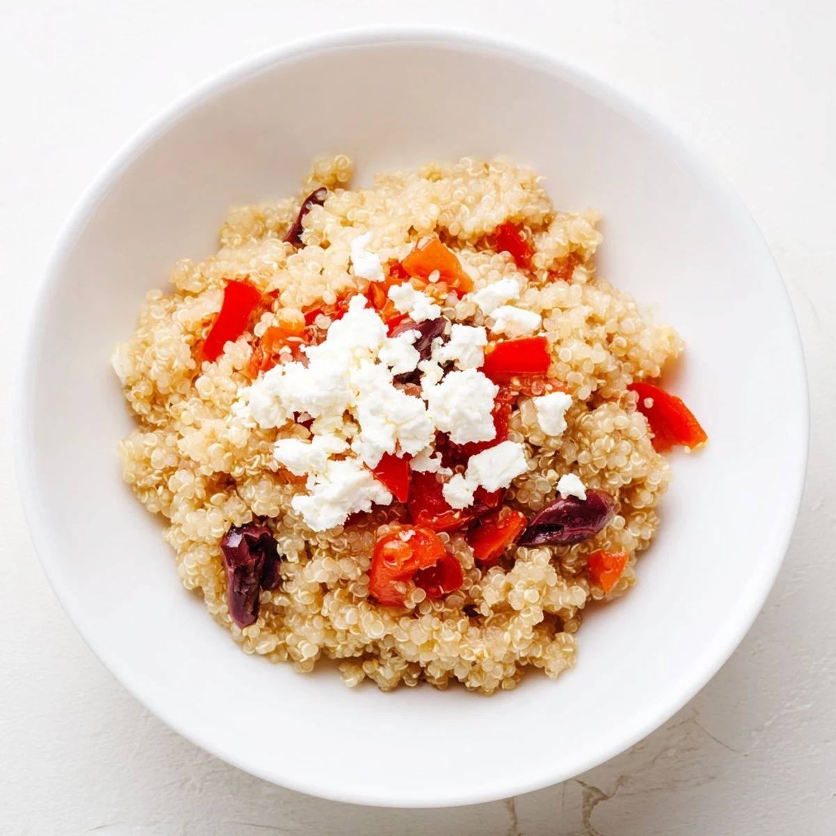 Fresh Mediterranean Quinoa Salad with Feta and Olives in a white bowl, colorful veggies and crumbled cheese glistening under a lemony dressing.