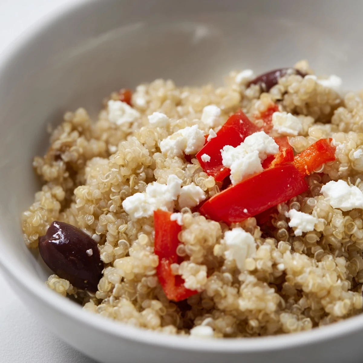 A vibrant Mediterranean Quinoa Salad with Feta and Olives, finished with a lemon-oregano dressing and extra black olives for briny flavor.