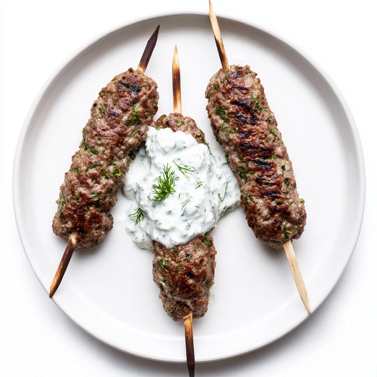 Spiced Middle Eastern beef kofta kebabs garnished with herbs and a side of creamy cucumber yogurt sauce.