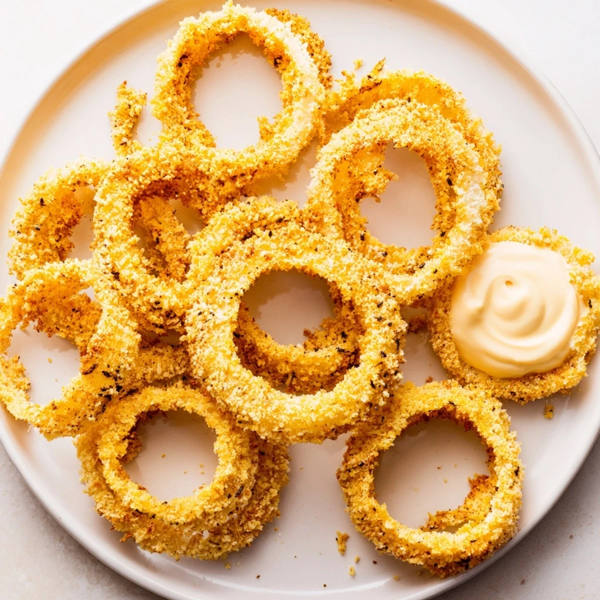 Panko-coated Crispy Air Fryer Onion Rings with Dip rest beside a ramekin of reddish dip on a plate.