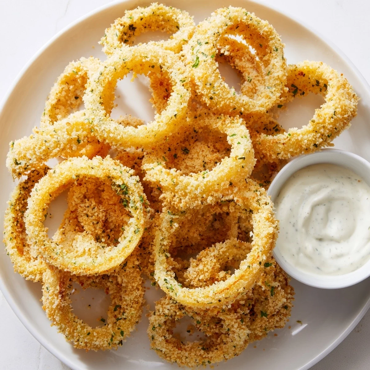 Golden, ultra-crispy Touchdown Crispy Onion Rings with Ranch arranged on a platter beside a small bowl of creamy dip.