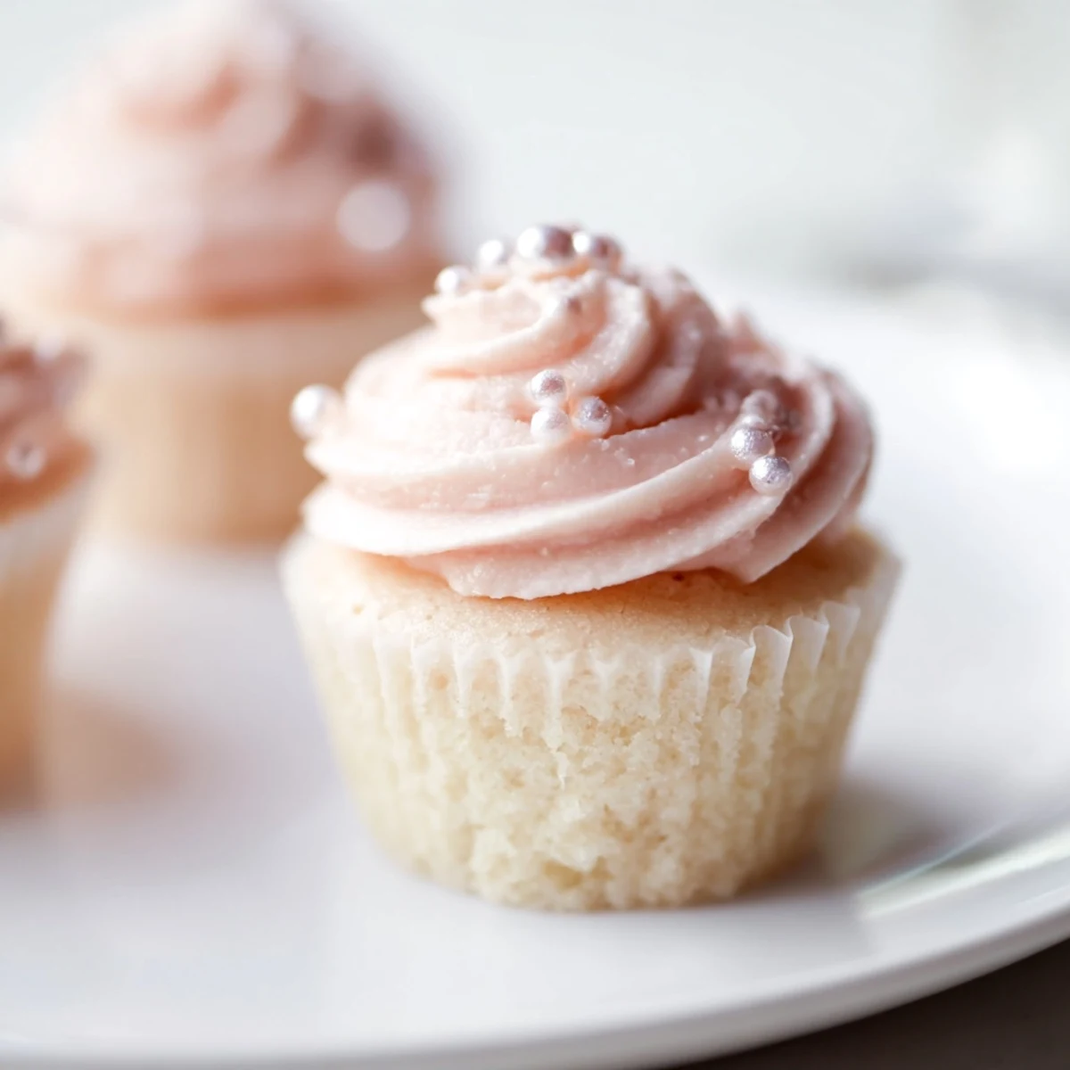 Freshly baked Pink Champagne Cupcakes with light pink buttercream and edible pearl sprinkles on a marble counter.
