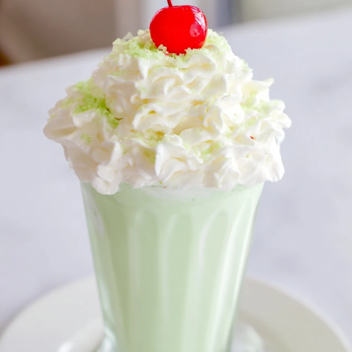 Shamrock Shake with Whipped Cream topped with fluffy cream and green sprinkles in a chilled glass.