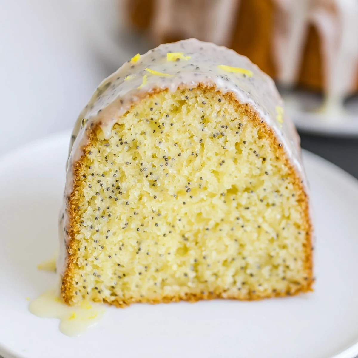 The golden-brown Lemon Poppy Seed Bundt Cake is sliced to reveal its fluffy interior, garnished with lemon zest and ready to serve with afternoon tea.