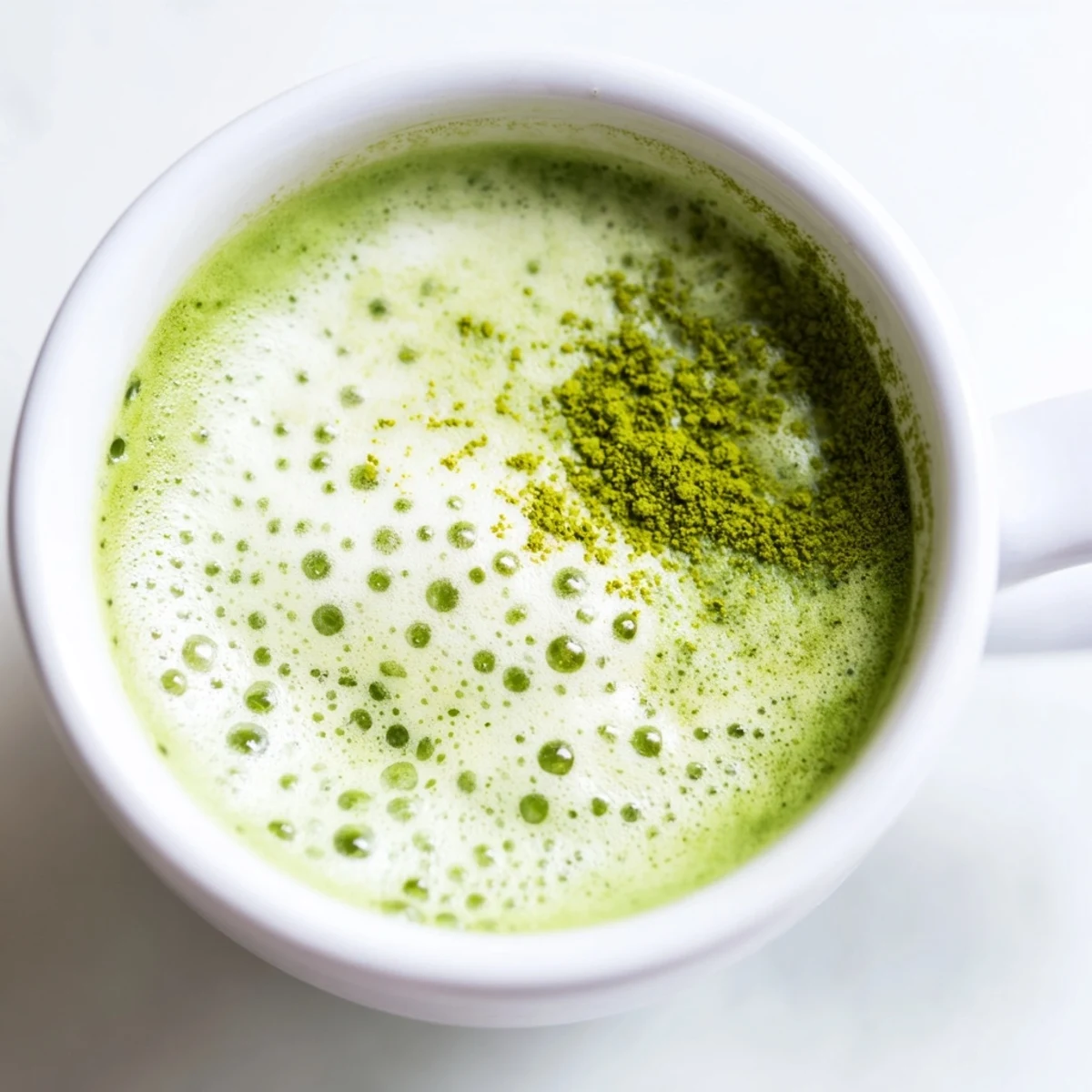 Creamy green matcha latte with almond milk served in a clear glass, showing a smooth, frothy top and vibrant color.  