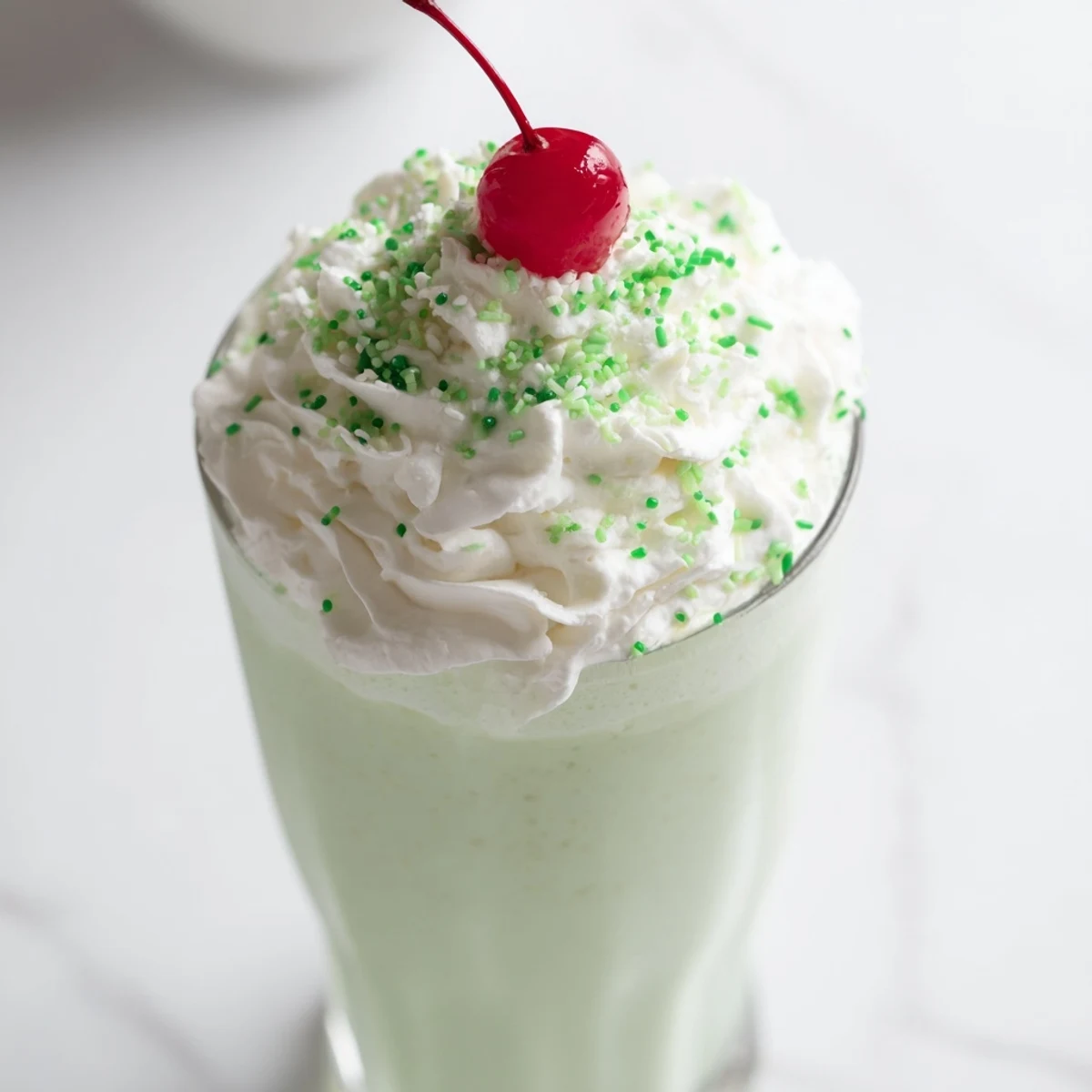 Two tall glasses of the Homemade Copycat Shamrock Shake are topped with fluffy whipped cream and a bright red maraschino cherry, reflecting a festive St. Patrick's Day vibe.