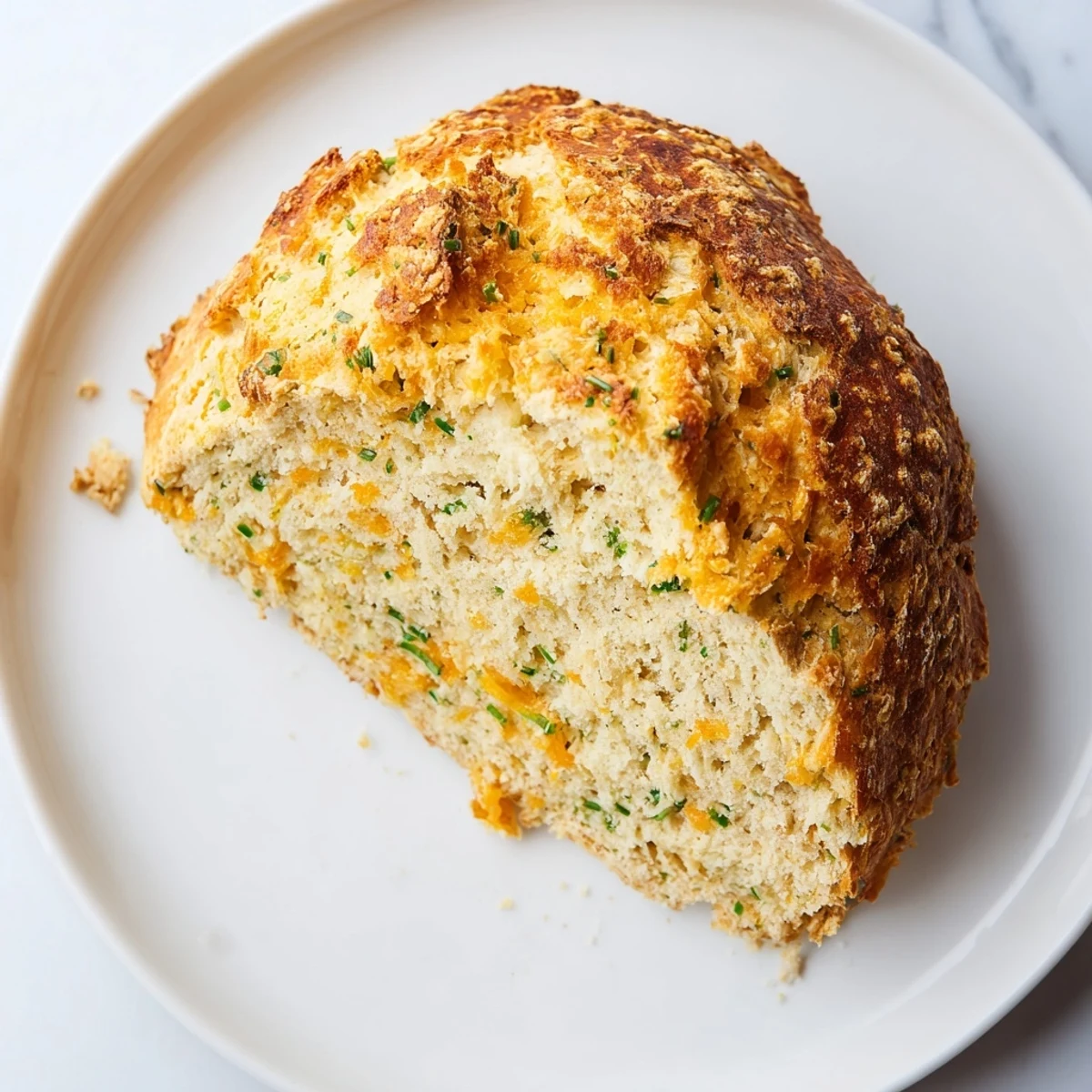 Savory Cheddar & Chive Irish Soda Bread loaf sliced open to show a tender, fluffy crumb studded with melted cheese.