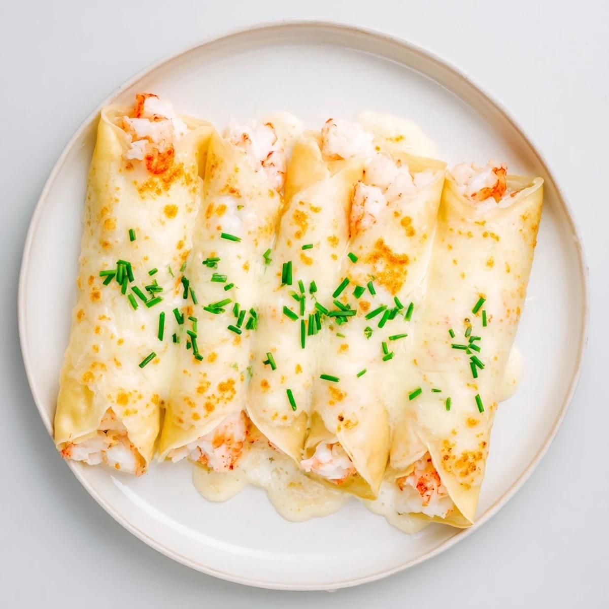 Golden-brown, folded Gourmet Seafood Crêpes filled with shrimp and crab, topped with creamy béchamel sauce and fresh chives.
