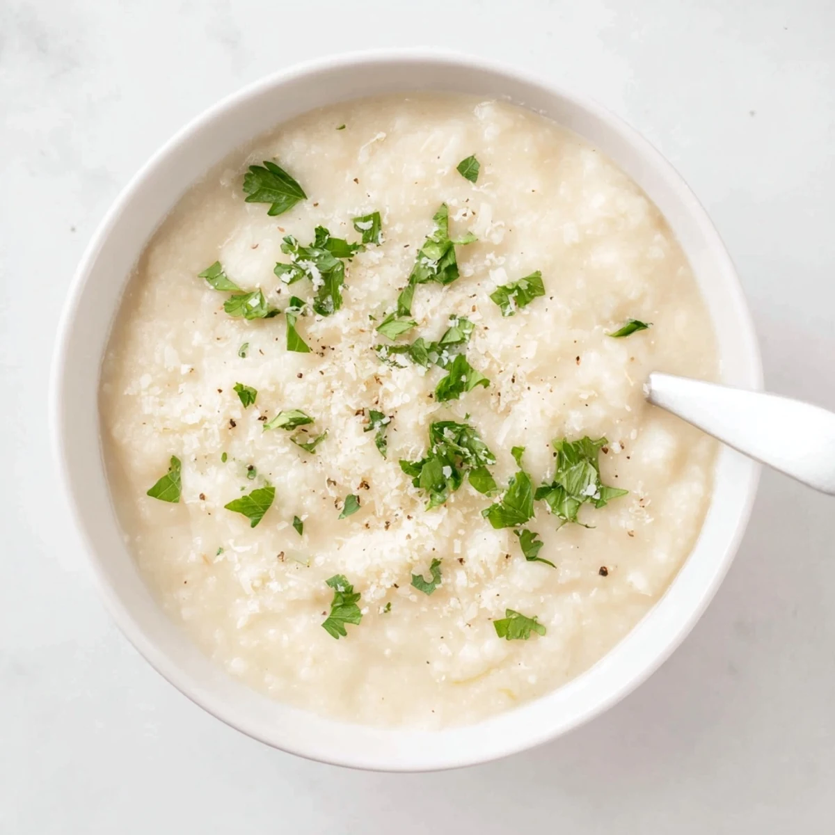 A warm bowl of Asiago Roasted Garlic Cauliflower Soup garnished with fresh parsley and melted Asiago cheese.  