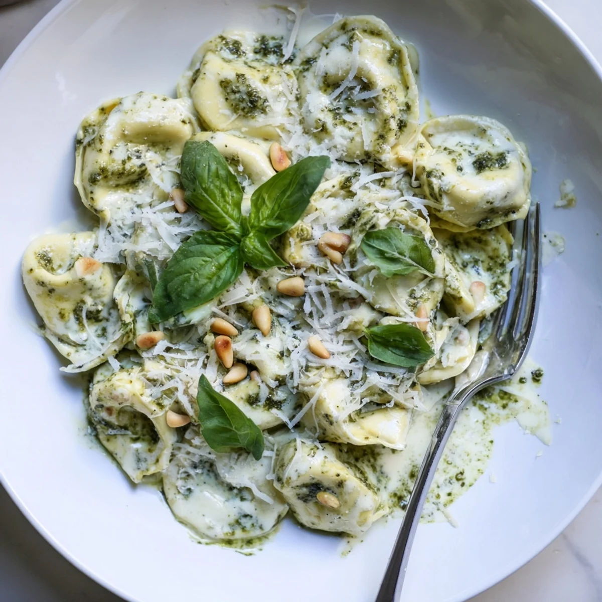 Creamy Pesto Alfredo Tortellini with fresh basil garnish and grated Parmesan, served in a white bowl.