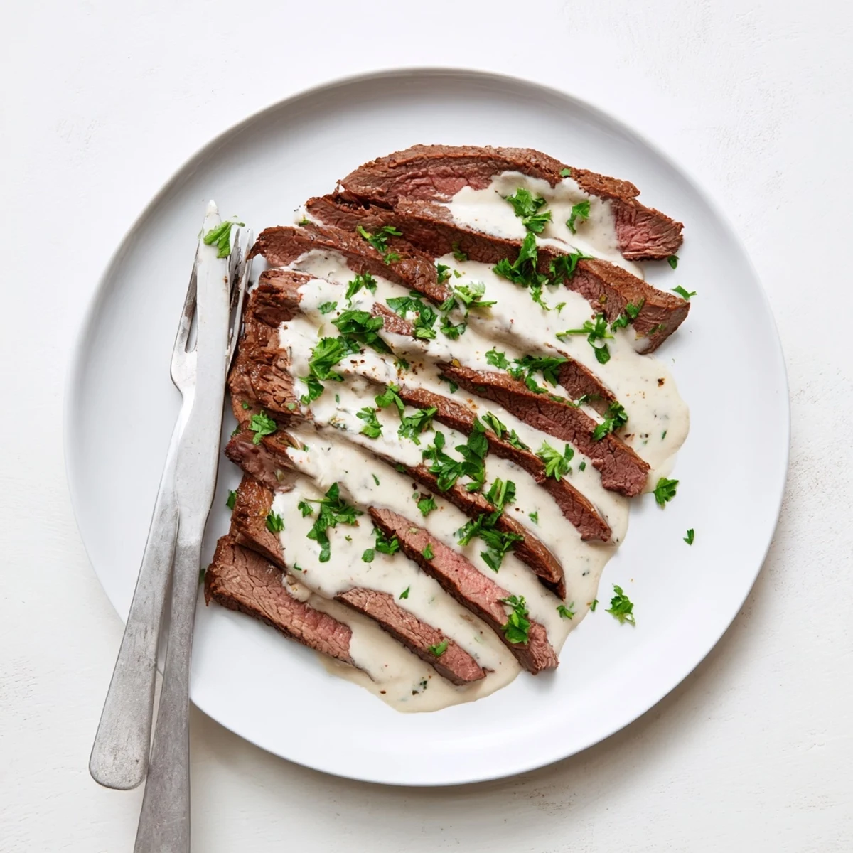 Perfectly rested flank steak with roasted garlic sauce plated alongside green beans, ready for a special weekend meal.