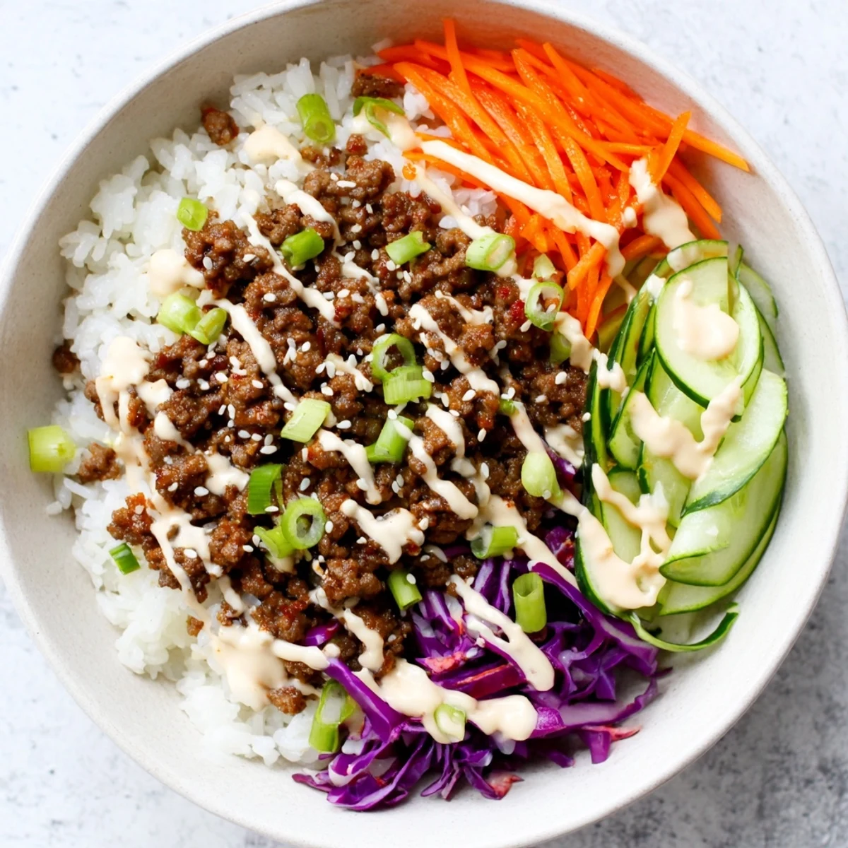 A close-up of Korean Beef Bowl with Spicy Mayo over fluffy rice, topped with crisp carrots and cucumber.