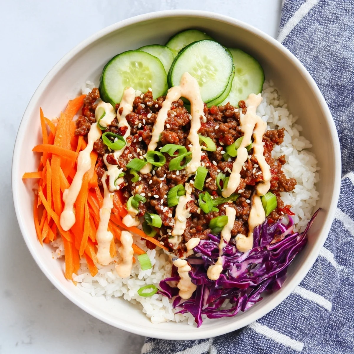 An overhead view of Korean Beef Bowl with Spicy Mayo, drizzled with creamy sauce beside pickled vegetables.
