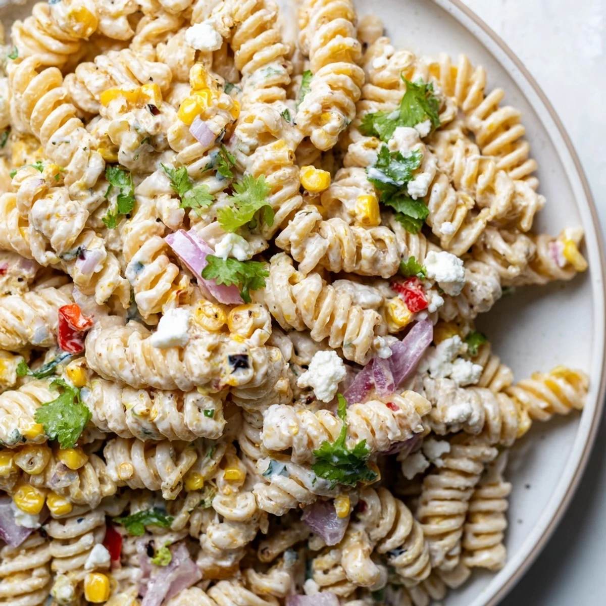 Serving bowl of Mexican street corn pasta salad garnished with fresh cilantro and crumbled white cheese