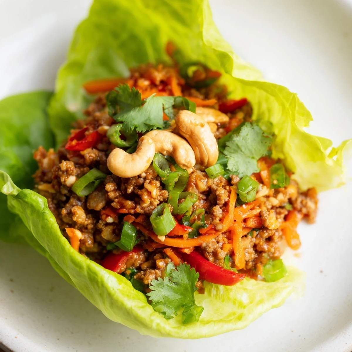 Garnished beef and cashew lettuce cups featuring crisp butter lettuce leaves topped with savory ground beef mixture, diced peppers, and fresh cilantro