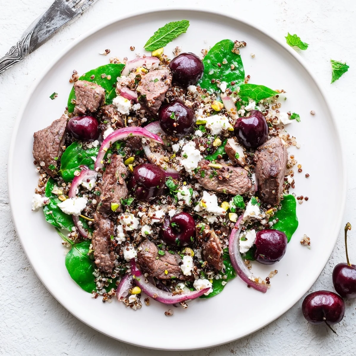 Mediterranean-inspired cherry quinoa salad with tender spiced lamb strips, juicy cherries, and crumbled feta in a serving bowl