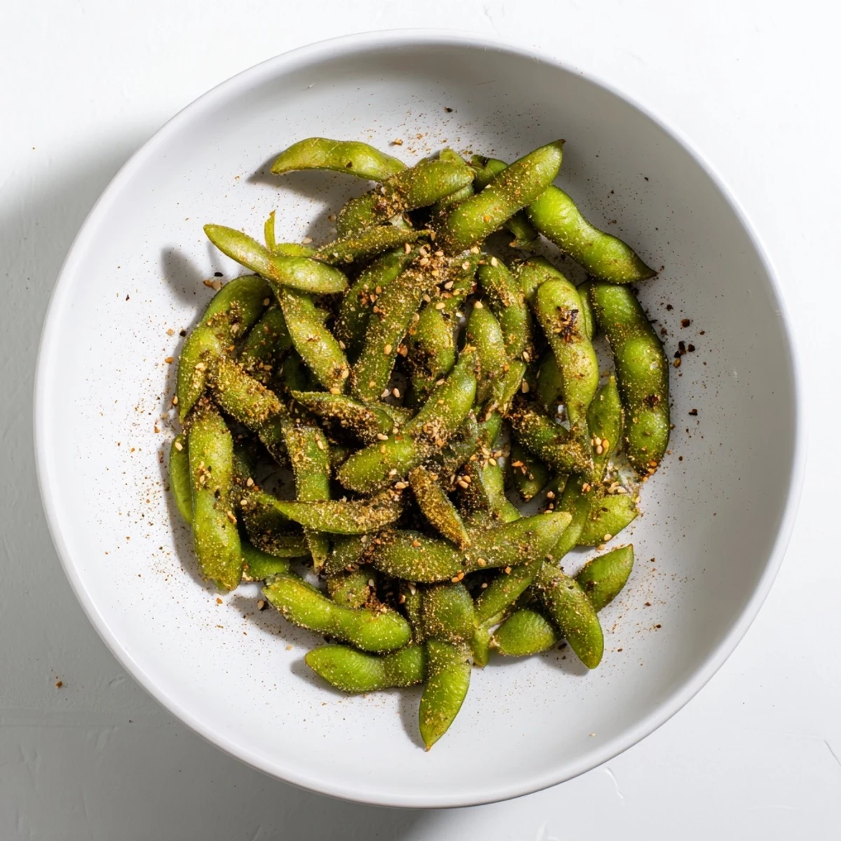 Crispy seasoned edamame beans steaming in a white bowl after air frying perfection