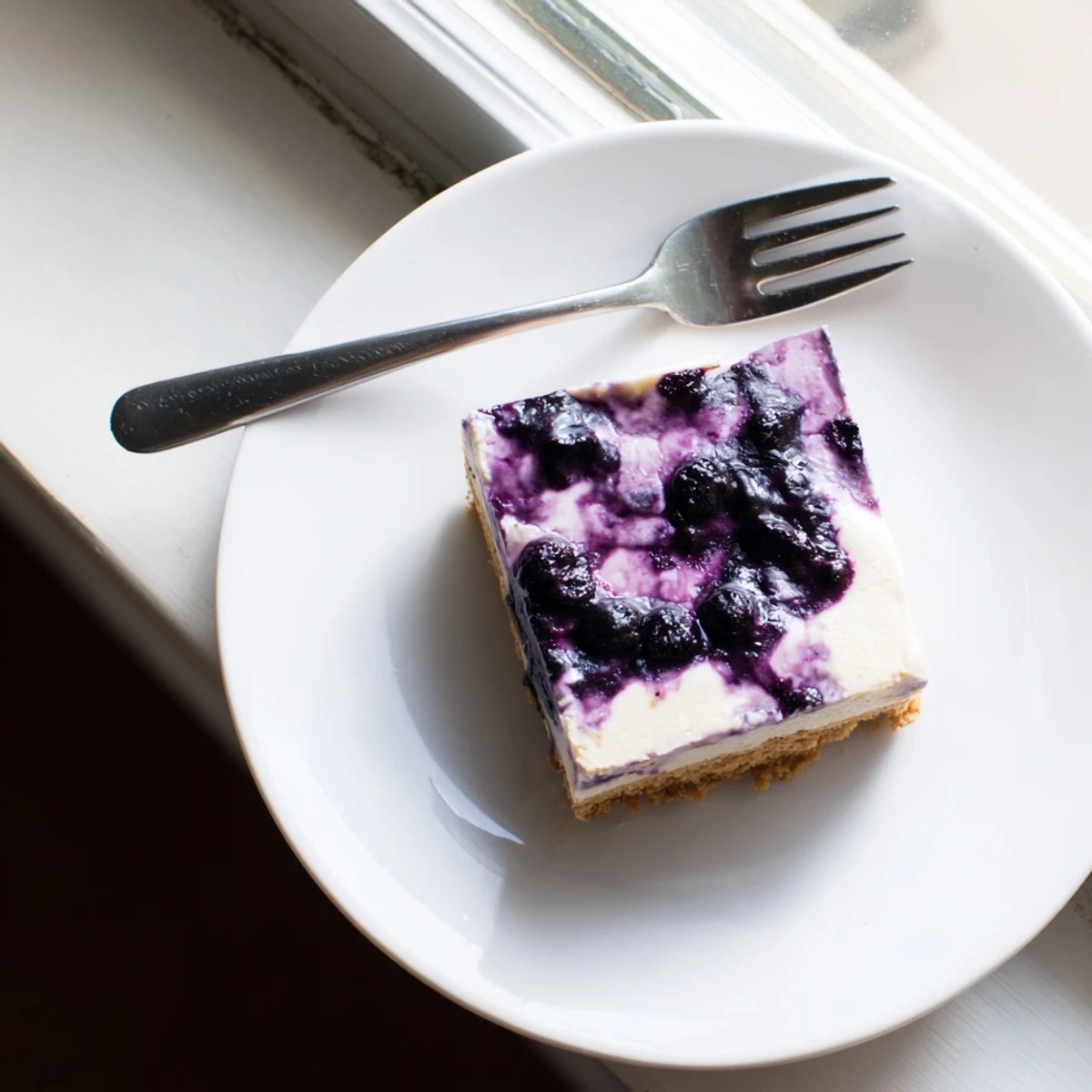 Rich blueberry cheesecake on a white plate featuring swirling blueberry sauce and buttery crust
