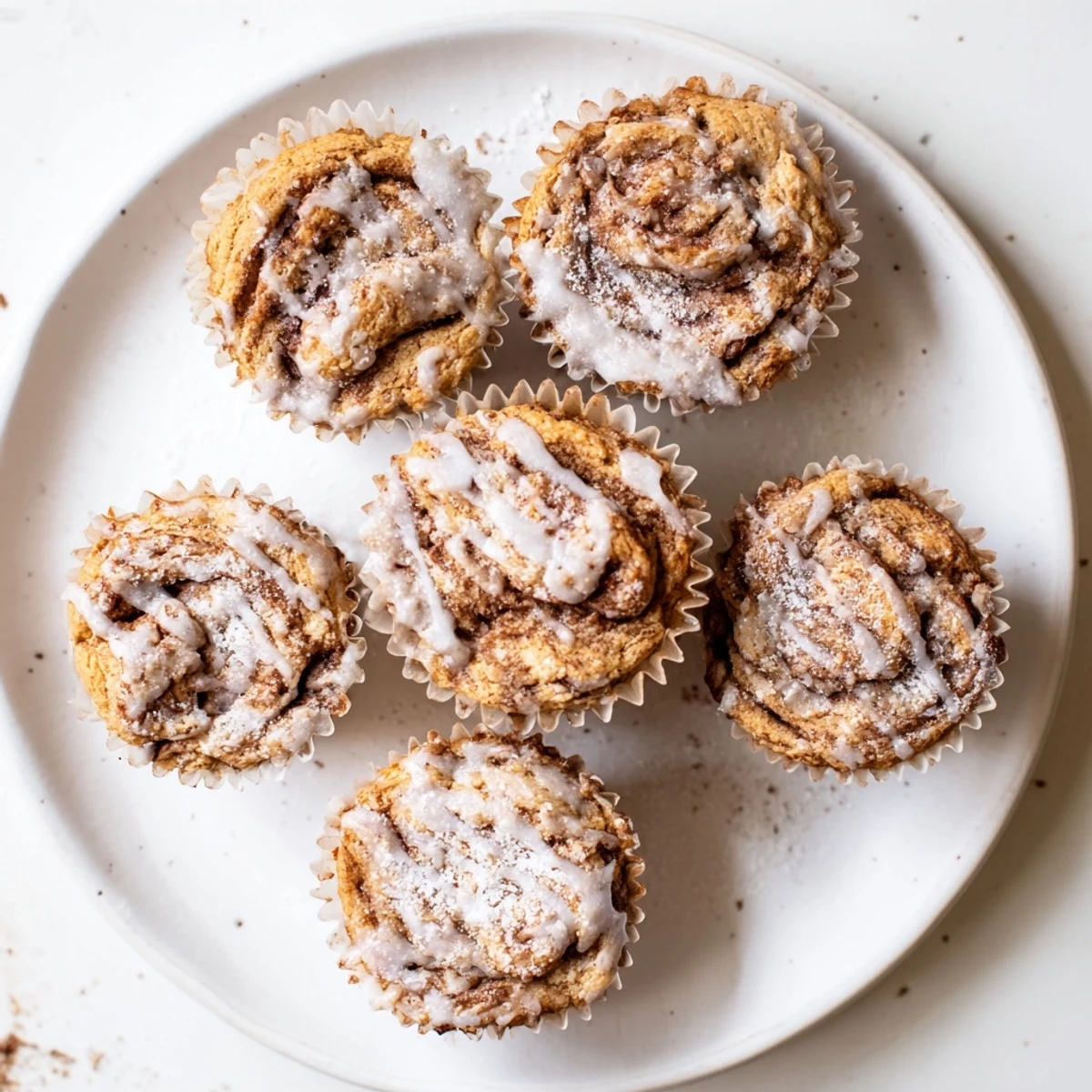 Golden brown cinnamon roll protein muffins topped with sweet white drizzle on a wire rack