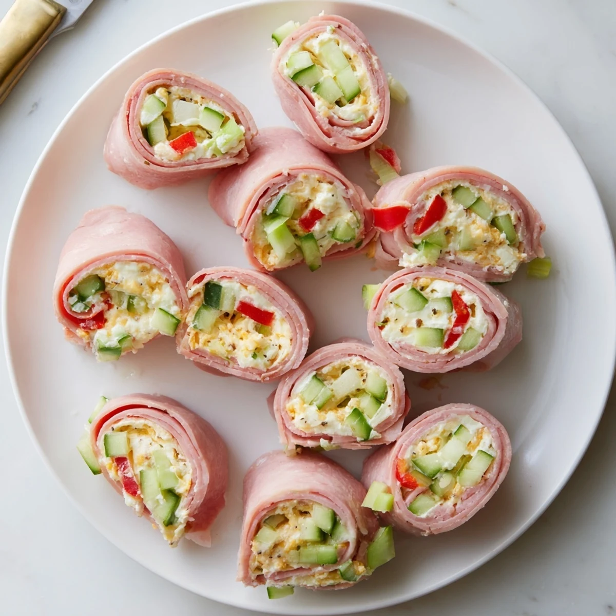 Creamy cheese-filled keto ham roll ups sliced in half revealing cucumber and red pepper inside