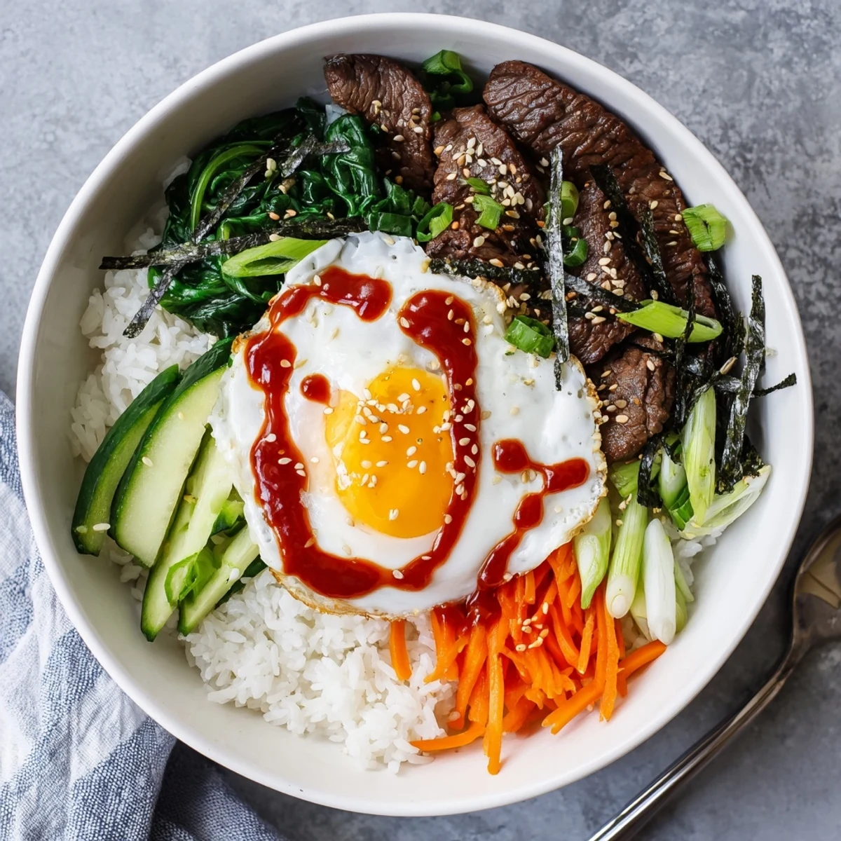 Korean-inspired breakfast bowl arranged with beef, sautéed vegetables, and sunny-side-up egg over steamed white rice