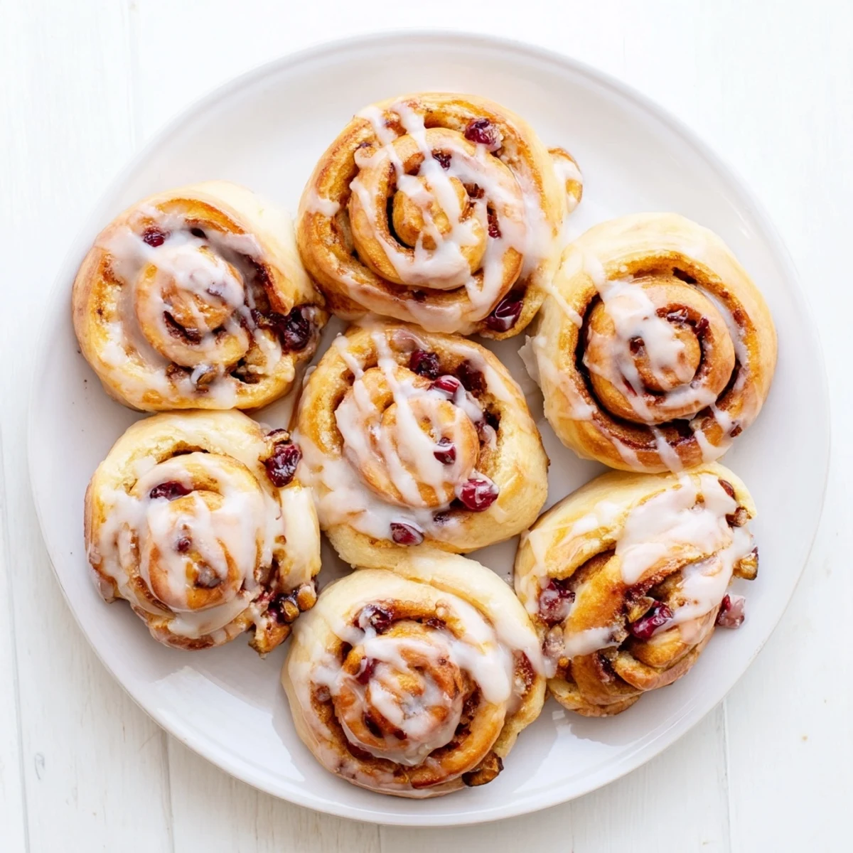 Freshly baked cherry cinnamon rolls with swirls of sweet cherries and vanilla glaze on a white plate
