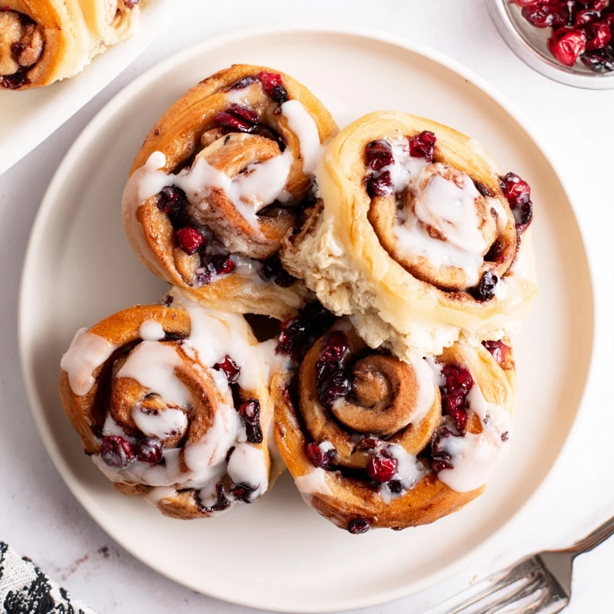 Golden cherry cinnamon rolls drizzled with white icing revealing red fruit spirals inside soft dough