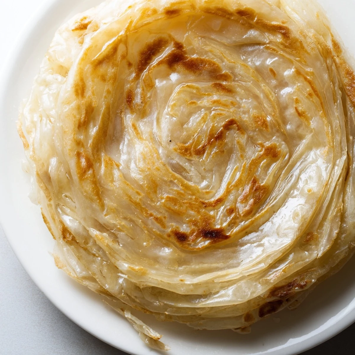 Golden flaky roti canai with layered Malaysian flatbread texture glistening with melted ghee