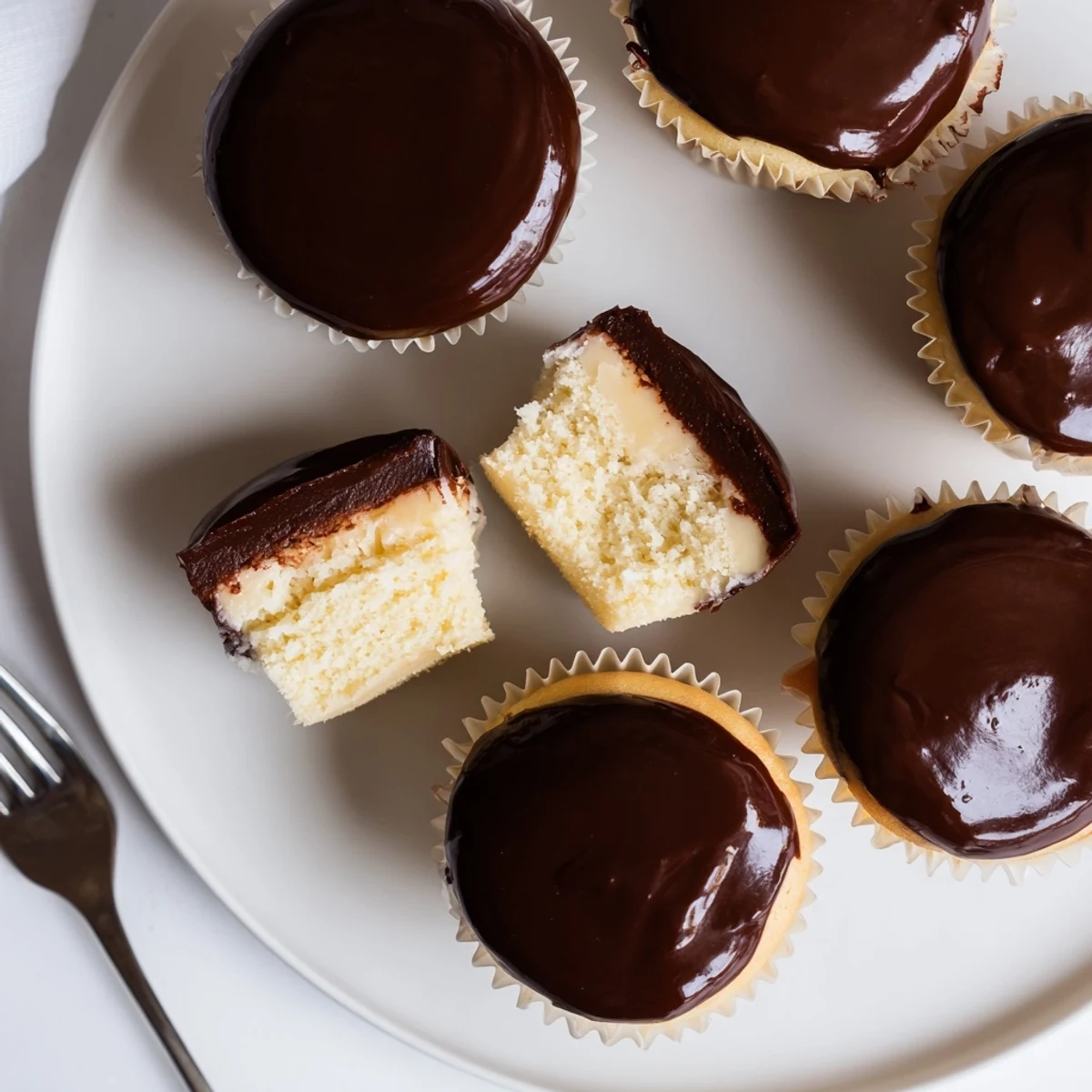 Golden Boston cream pie cupcakes with vanilla cake and creamy pastry filling crowned with glossy chocolate ganache topping