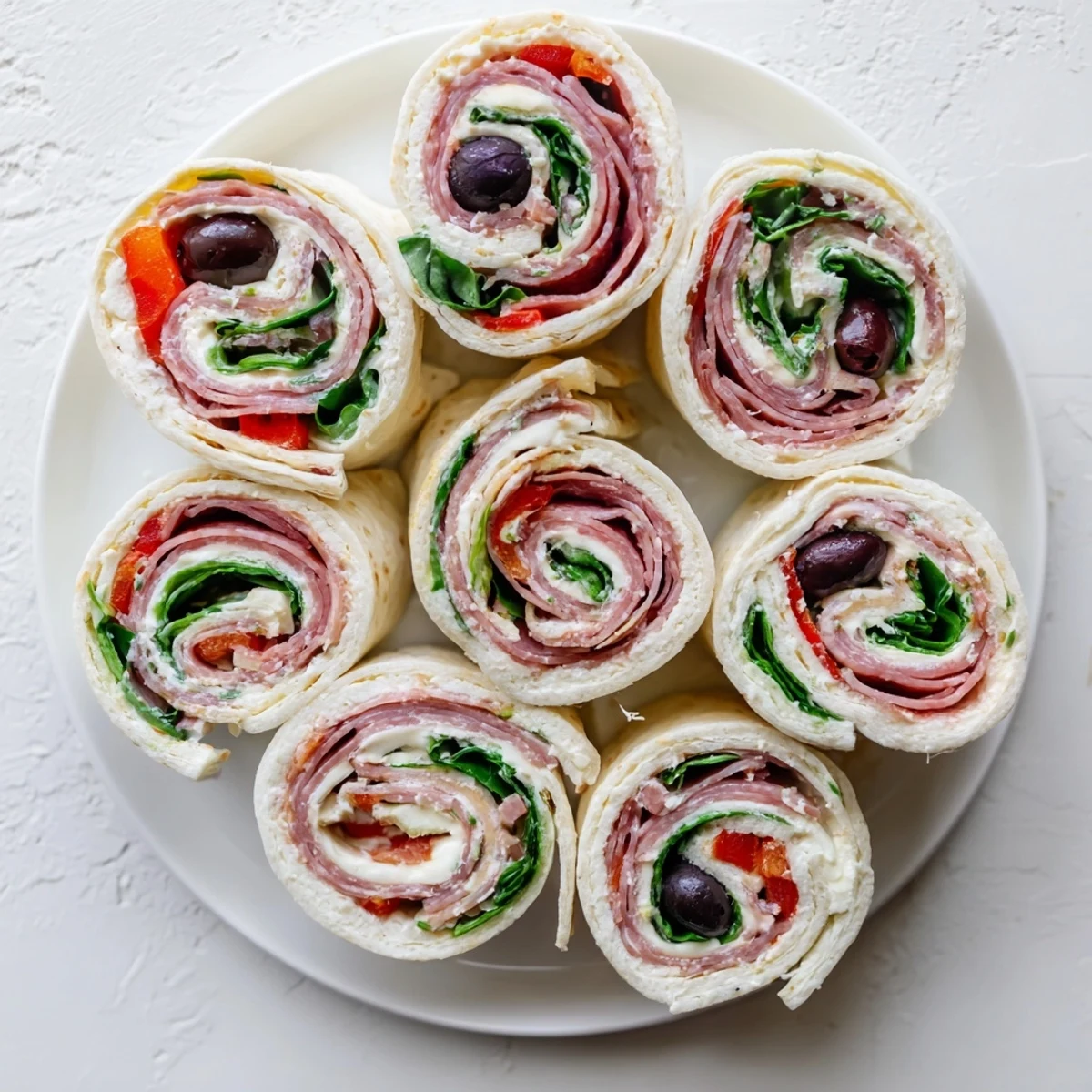 Colorful Italian pinwheel sandwiches arranged on a serving platter with fresh spinach and black olives