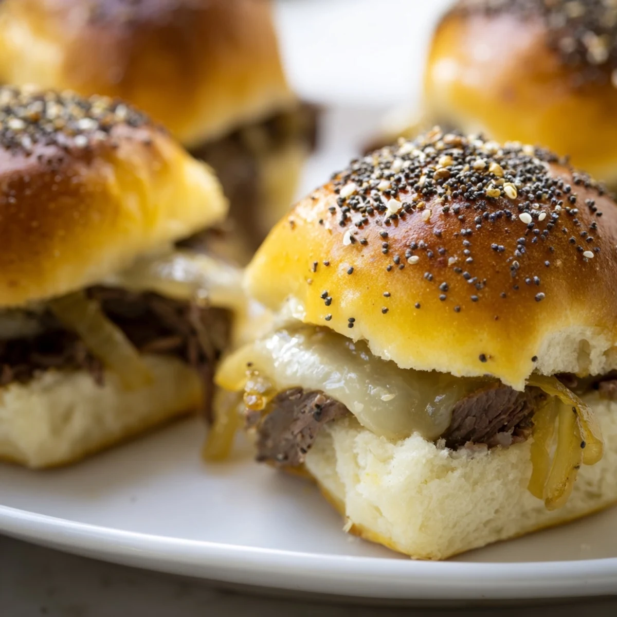 Baked French dip sliders brushed with garlic butter and poppy seeds, ready for dipping into savory beef broth