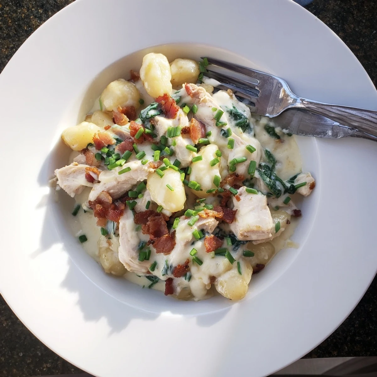 Golden gnocchi swimming in rich cream sauce with chicken pieces bacon and wilted green spinach