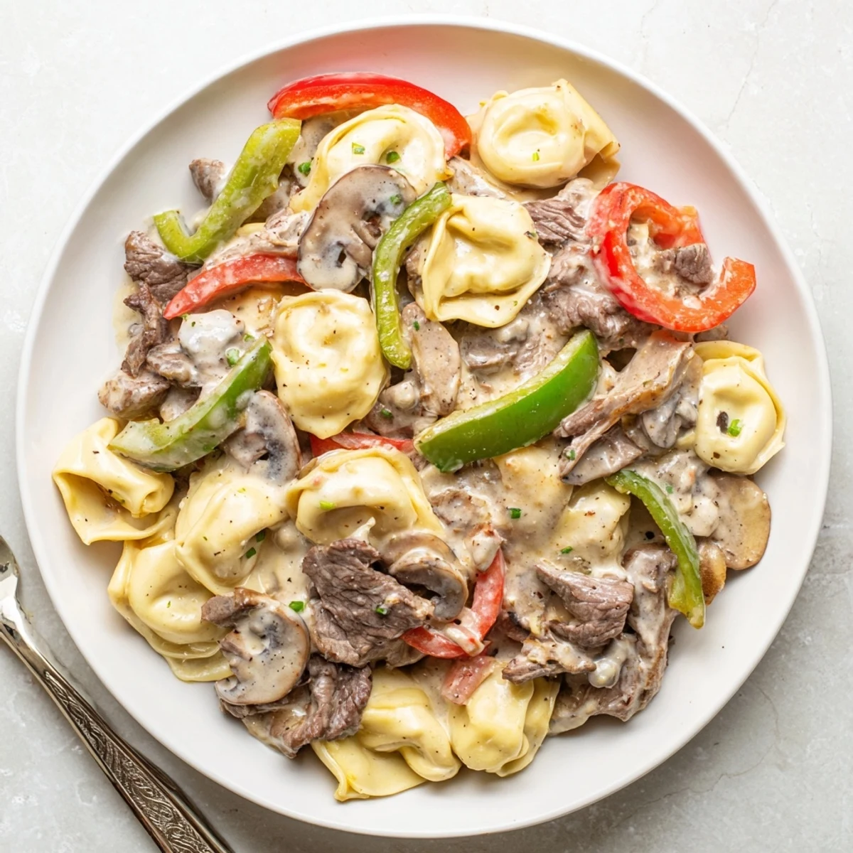 Spoonful of Crock Pot cheesesteak tortellini showing beef, mushrooms, and gooey melted cheese in a comforting bowl