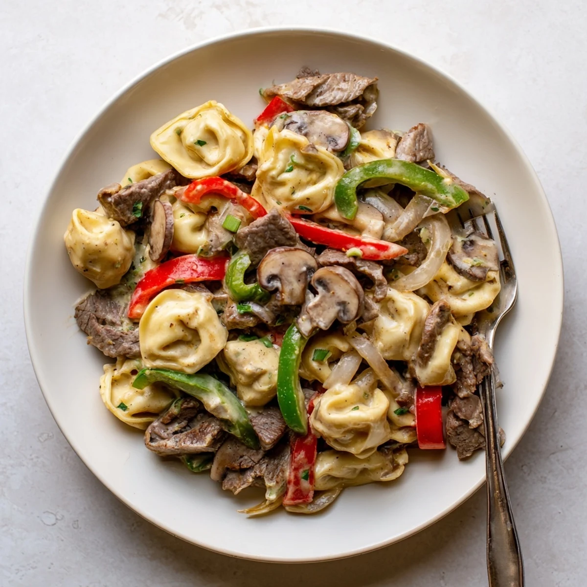 Hearty slow cooker cheesesteak tortellini featuring savory steak, colorful vegetables, and cheesy tortellini in rich cream sauce