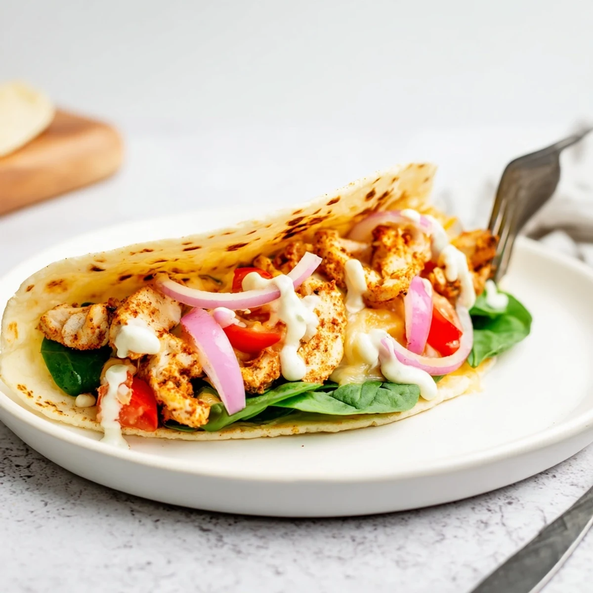 Warm low carb tortilla packed with grilled chicken spinach tomatoes and creamy garlic sauce