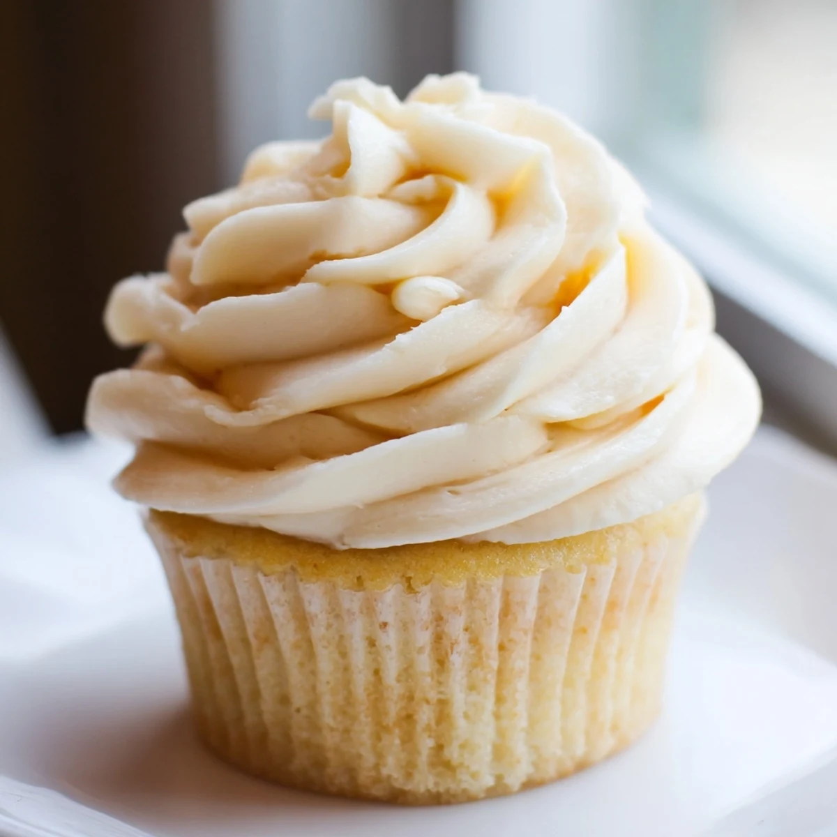 Fluffy vanilla cupcakes topped with creamy vanilla buttercream frosting and colorful sprinkles on a white plate