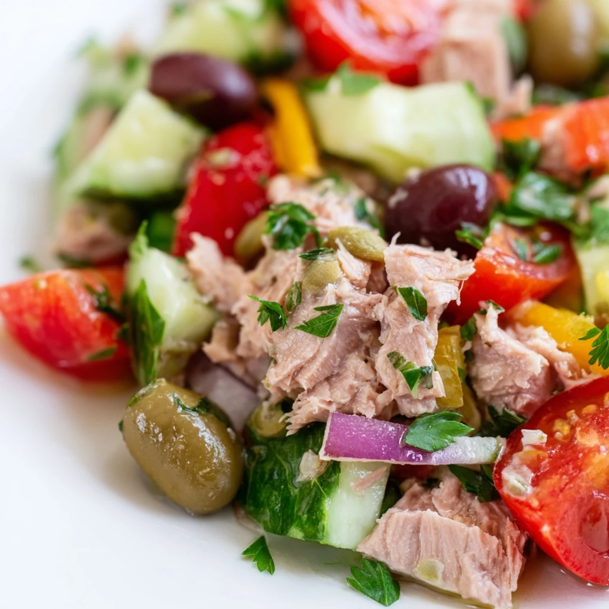 Mediterranean tuna salad in a white bowl with cherry tomatoes, olives, and fresh parsley