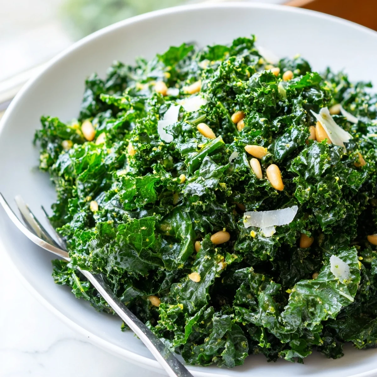 Fresh massaged kale leaves glistening with zesty garlic lemon Parmesan dressing topped with pine nuts