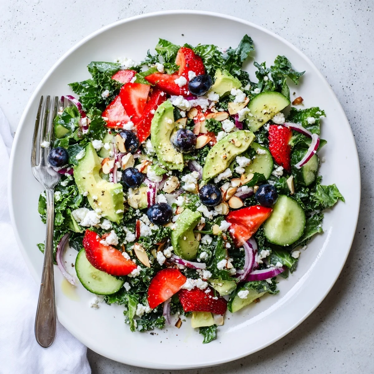 A colorful summer kale salad topped with strawberries, feta, and toasted almonds