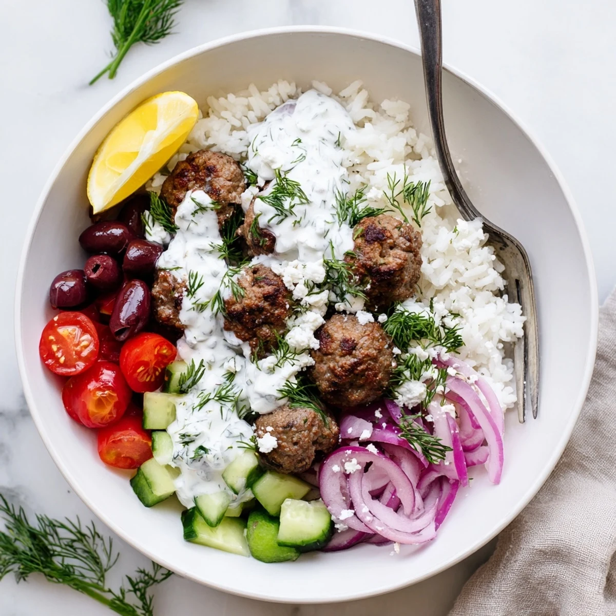 A vibrant Greek meatball bowl drizzled with creamy tzatziki alongside a lemon wedge