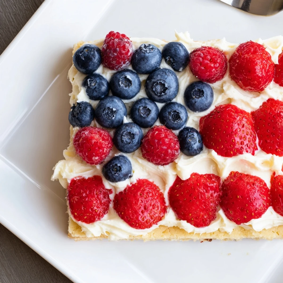 Sliced Sugar Cookie Flag Fruit Pizza on parchment, creamy frosting, juicy berries.