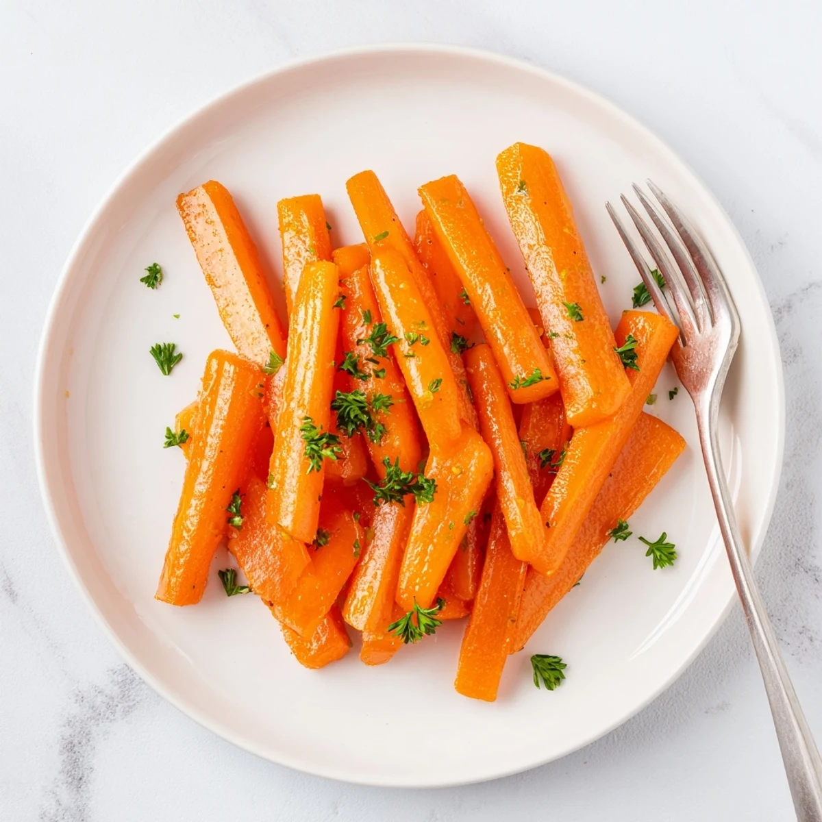 Golden honey glazed carrots glistening on a white serving plate with fresh parsley sprinkles