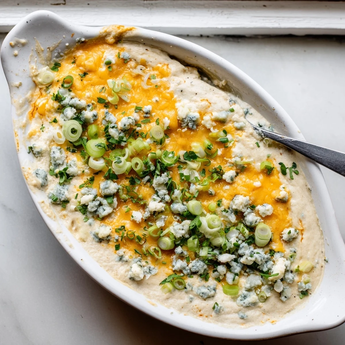 Golden cheesy white bean buffalo dip bubbling hot with melted cheddar and crumbled blue cheese topping