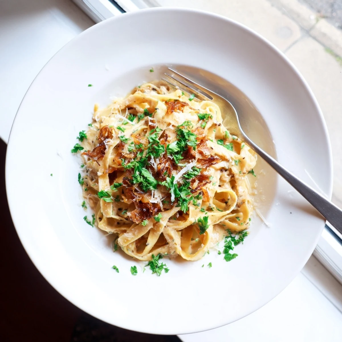Steaming bowl of caramelized onion cream pasta garnished with fresh parsley and extra cheese