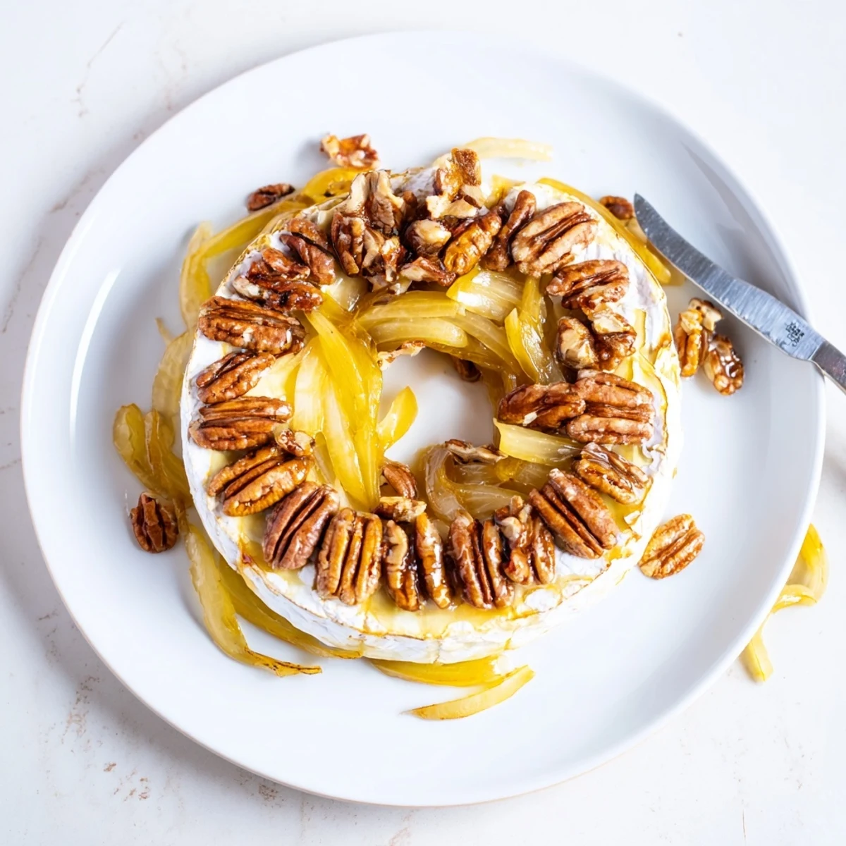 Golden baked brie wheel oozing creamy cheese topped with sweet caramelized onions and toasted pecans