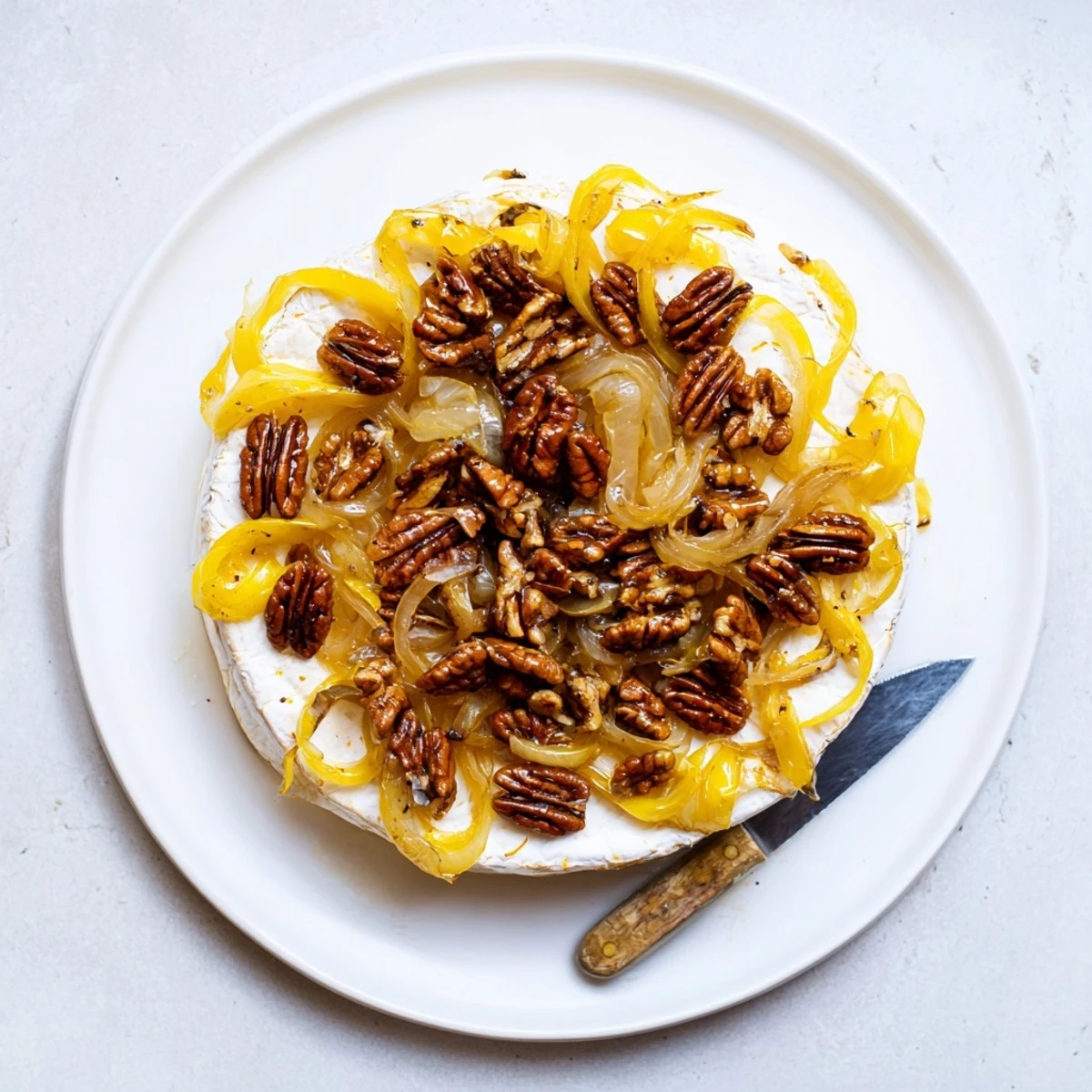 Decadent baked brie with rich caramelized onions and crispy pecans served on rustic wooden board